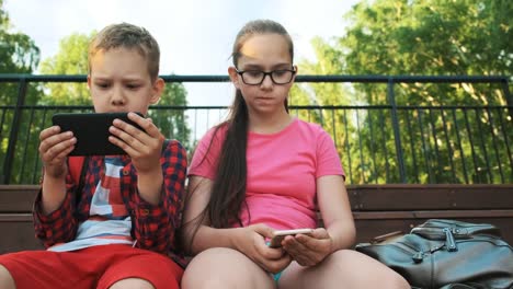 Die-ältere-Schwester-und-der-Bruder-sitzen-auf-der-Straße-und-schauen-auf-Smartphones.