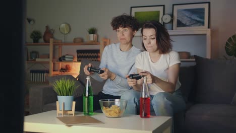 Beautiful-girls-playing-video-game-at-home-at-night-having-fun-sitting-on-sofa