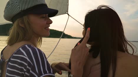 young-lesbian-woman-touching-hair-of-her-partner-on-sailboat-at-sunset