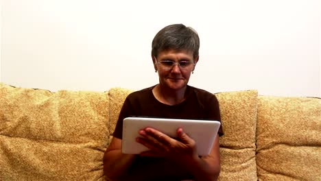 Attraktive-erwachsene-Frau-arbeiten-auf-ihrem-Tablet,-während-auf-einem-Sofa-zu-Hause-sitzen.