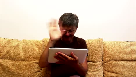 Eine-attraktive-erwachsene-Frau-ist-Video-Chat-mit-ihrer-Familie,-auf-einem-Tablet-PC,-sitzen-auf-einem-Sofa-zu-Hause.