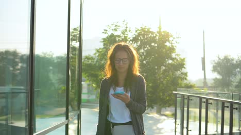 Mujer-caminando-frente-al-sol.-La-chica-está-viendo-el-mensaje-en-las-redes-sociales.-Cámara-lenta