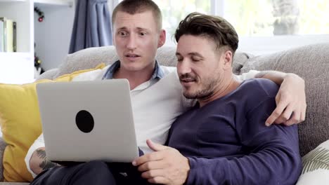 Gay-couple-relaxing-on-couch-using-laptop-computer.-Talking-exciting.