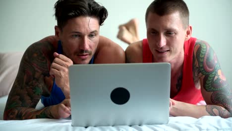 Gay-couple-in-bed-using-laptop-computer.-Focus-on-display.