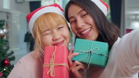 Pareja-lesbiana-asiática-celebran-festival-de-Navidad.-LGBTQ-adolescente-mujer-relajarse-feliz-sosteniendo-regalo-y-el-uso-de-selfie-smartphone-con-árbol-de-Navidad-disfrutar-de-las-vacaciones-de-invierno-de-Navidad-en-la-sala-de-estar-en-casa.