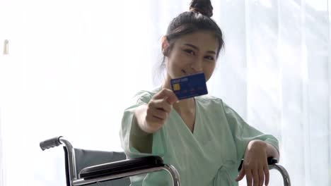 Happy-patient-hold-credit-card-and-smile-while-sitting-on-wheelchair-at-hospital