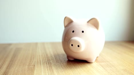 Man's-hand-putting-coins-in-piggy-bank-of-pig-shape-on-the-table,-closeup