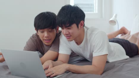 Asian-Gay-lgbtq-men-couple-using-computer-laptop-at-modern-home.-Young-Asia-lover-male-happy-relax-rest-together-after-wake-up,-watching-movie-lying-on-bed-in-bedroom-at-house-in-the-morning-concept.