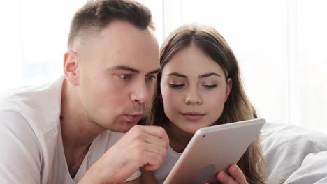 Astonished-couple-using-digital-tablet-in-bed