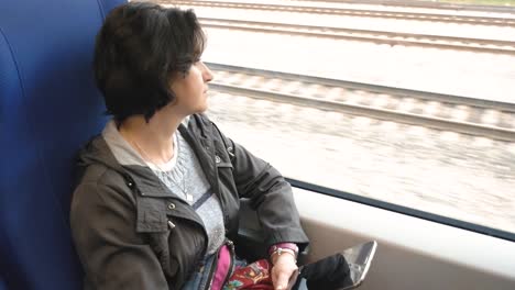 Caucasian-woman-rides-in-a-train-sitting-by-window-with-a-tablet-in-her-hands