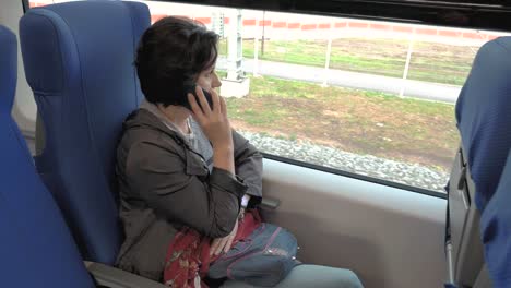 a-woman-is-sitting-on-a-train-talking-on-the-phone