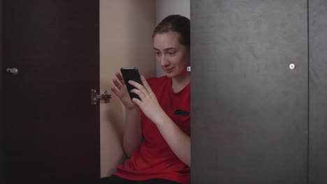 Soccer-Girl-in-Sports-Uniform-Sitting-in-Locker-and-Using-Smartphone