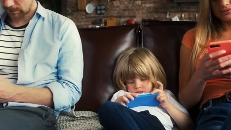 Young-father,-mother-and-their-child-boy-in-casual-clothes-are-using-smartphones-while-sitting-on-couch-in-living-room.-Close-up,-slow-motion