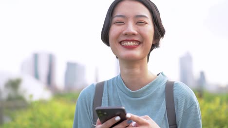 Close-up-face-of-asian-woman-using-smart-phone.-Happy-female-face-with-white-teeth-pretty-face-posing-for-close-up-portrait-outdoor.