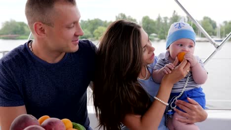 los-padres-con-el-niño-en-yate,-niño-come-primer-alimento-en-las-madres-de-las-manos-en-reposo,-amor-de-pareja-junto-con-bebé-pequeño