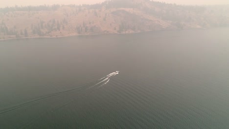 Aerial-Above-Eastern-Washington-Lake-with-Boat-Towing-Inner-Tubes-in-Wildfire-Smoke