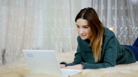 Pretty-girl-lays-on-the-carpet-on-floor-and-uses-laptop