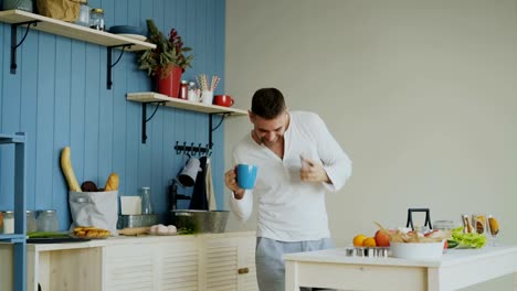 Cheerful-happy-man-dancing-and-singing-in-kitchen-while-using-his-smartphone-at-home-in-the-morning