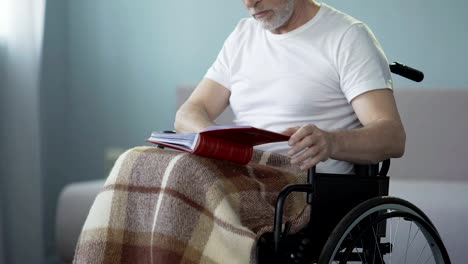 Old-age-man-with-disabilities-reviewing-album-with-photos,-missing-relatives