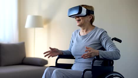 Impressed-grandmother-in-wheelchair-wearing-goggles,-playing-VR-game,-device