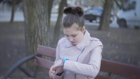 Mädchen-Teenager-sitzen-auf-einer-Bank-im-freien-und-ist-smart-Watch