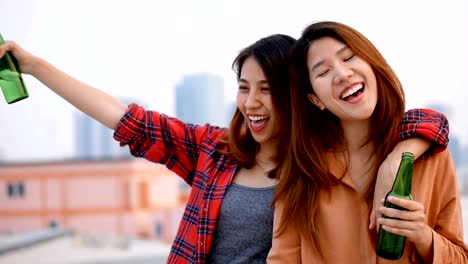 Slow-motion-young-asian-woman-lesbian-couple-clinking-bottles-of-beer-party-on-rooftop.