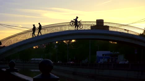 siluetas-de-personas-que-cruzan-el-canal-en-un-puente-jorobado