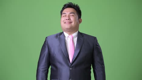 Young-handsome-overweight-Asian-businessman-against-green-background