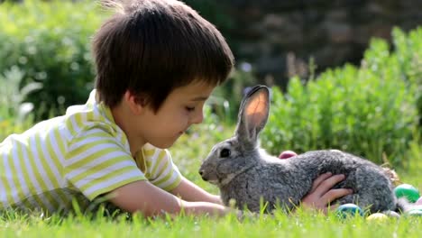 Niedlichen-Kind,-spielt-mit-kleinen-Häschen-und-Ostern-Eier-in-einen-blühenden-Garten,-Frühling.-Junge-mit-Kaninchen-spielen,-Ei-Jagd-für-Urlaub