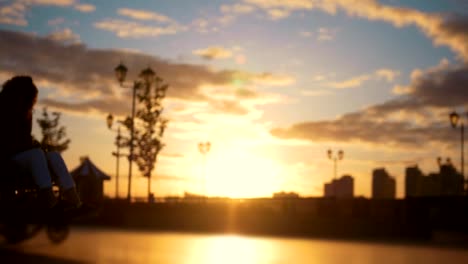 Caring-man-with-a-disabled-woman-in-wheelchair-walking-through-the-quay-at-sunset