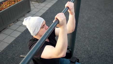 Muscular-disabled-man-in-wheelchair-pulls-up-on-the-crossbar-outdoors