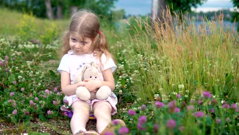 Ein-kleines-Mädchen-spielen-mit-einem-Spielzeug-Hasen-auf-der-Wiese-unter-den-blühenden-Klee