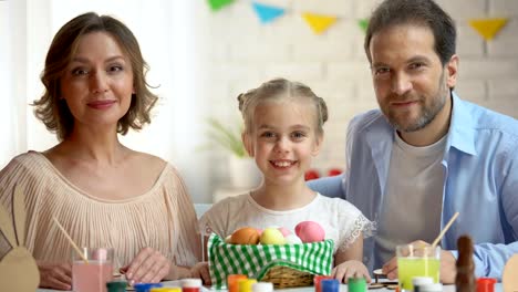 Friendly-family-posing-at-camera-with-basket-of-brightly-colored-Easter-eggs