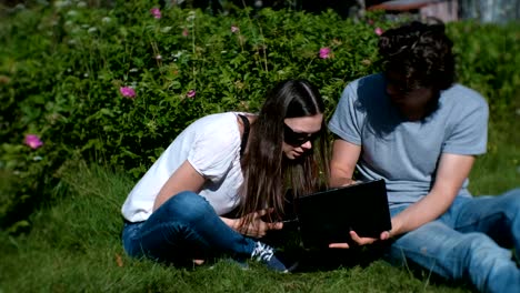 Junges-Paar-Mann-und-Frau-arbeiten-zusammen-auf-Handy-und-Laptop-im-Park-sitzen.