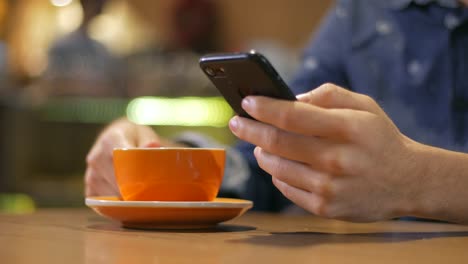 Nahaufnahme-der-Hände-eines-Mannes-mit-Smartphone-und-trinken-aus-einer-dampfenden-Tasse-Kaffee-in-einem-Café-in-Medellin-Kolumbien