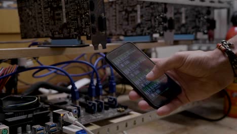 Technician-man-showing-mining-software-progress-on-smartphone-display-near-the-gpu-cryptocurrency-mining-rig