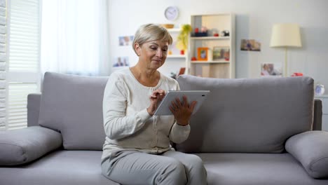 Señora-Senior-de-compras-en-línea-en-la-tableta-en-casa-sonriendo-a-la-cámara,-tecnología