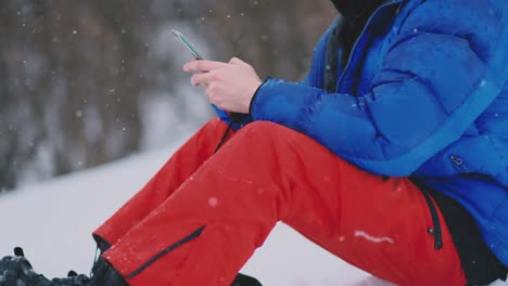 Männliche-Snowboarder-sitzen-auf-dem-Schnee-und-machen-Fotos-am-Telefon-schöne-Landschaft-des-Resorts-für-soziale-Netzwerke