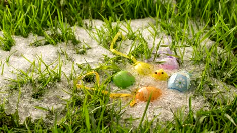 Snow-is-melting-in-green-grass-meadow-with-colorful-Easter-eggs-and-little-chick-decoration-Time-lapse