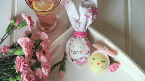 Close-up-Easter-eggs-decorated-for-Easter-bunny-and-Easter-chick-with-painted-muzzle,-against-background-of-pink-carnations-and-lemonade-with-lemon