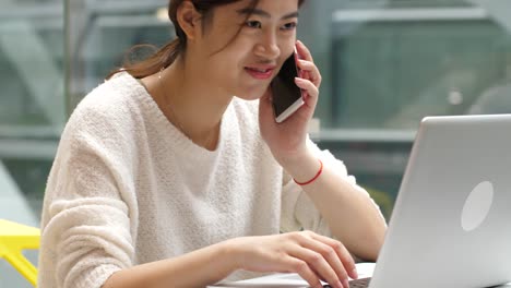 mujer-asiática-muy-joven-con-teléfono-móvil-y-portátil-en-el-interior