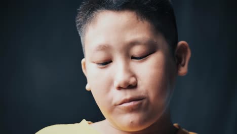 large-build-Asian-preteen-boy-eating-donut-while-touching-his-tummy,-slow-motion-in-low-light.