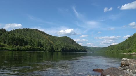 Scenic-summer-mount-landscape-with-fast-moving-clouds-above-river-and-boats