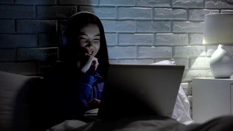 Smiling-woman-in-headphones-watching-video-at-night,-addiction-to-social-media