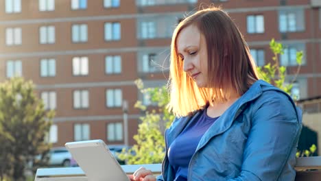 Woman-using-tablet-computer-sitting-on-bench-in-city