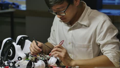 Young-asian-electronics-development-engineers-building,-testing,-fixing-robotics-in-computer-science-research-laboratory-at-night.-People-with-technology-or-innovation-concept.