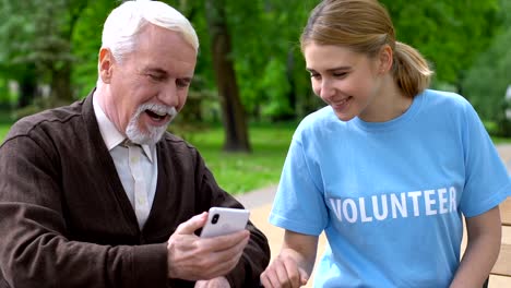 Freundliche-weibliche-Freiwillige-hilft-Rentnerin-im-Rollstuhl-verwenden-Smartphone-Charity-App