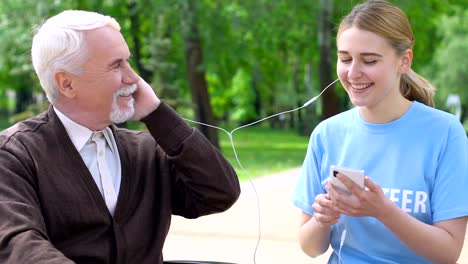 Mujer-voluntaria-dando-auriculares-a-un-viejo-solitario,-escuchando-música-en-el-parque