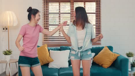 Asian-Lesbian-couple-happy-fun-dance,-singing,-listening-music-while-in-living-room-at-home.