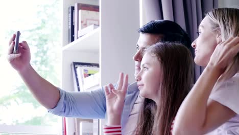 Familia-riendo-y-buscando-selfie-en-el-teléfono-inteligente-en-la-sala-de-estar